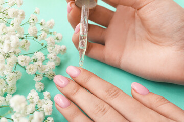 Female hands with cuticle oil and gypsophila flowers on color background, closeup