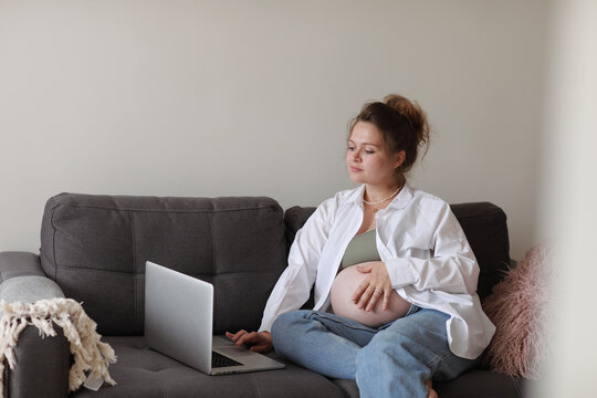 Attractive pregnant young lady working remotely online from home office. Close up woman hands on laptop with big belly advanced pregnancy. selective focus.