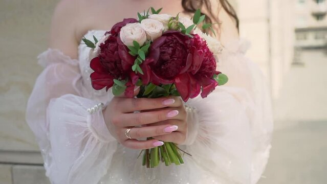 Female in dress hold in hands bouquet with ribbons of red peony flowers. Gift for a woman, holiday, wedding bouquet of the bride. Floristics. Outdoors in summer.