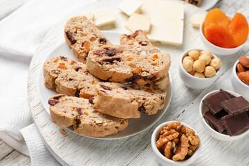 Board with tasty biscotti cookies, nuts, chocolate and dried apricots on table, closeup