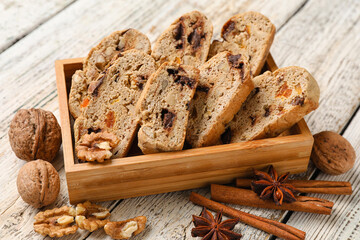 Basket with tasty biscotti cookies, spices and walnuts on light wooden background, closeup