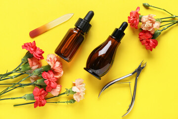 Composition with bottles of cuticle oil, manicure instruments and carnation flowers on yellow background