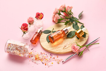 Composition with bottles of cuticle oil, sea salt and beautiful rose flowers on pink background