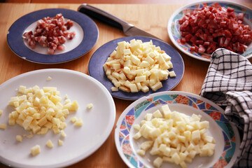 Some basic ingredients cut for the filling of a savory pie (salami, bacon, cheeses) arranged in plates on a wooden chopping board