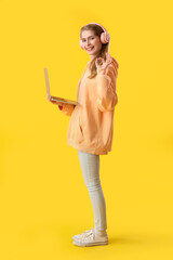 Fototapeta premium Female programmer in headphones with laptop showing OK on yellow background