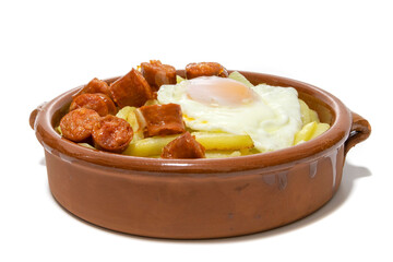 Chistorra with fried potatoes and fried eggs, served in a clay bowl (Chistorra, is a type of sausage of Navarre origin made with fresh minced pork.Isolated in a white background. Spanish food concept.