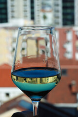 A glass of white wine with city view. Reflection of the city in the glass of white wine. Close up of a transparent glass of white wine in front of the city landscape