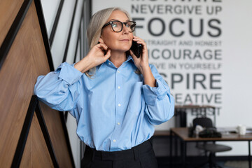 mature adult female economist with gray hair in office clothes speaks on the phone