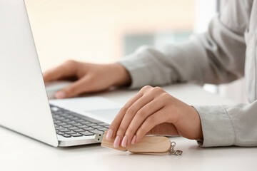 Woman with modern laptop and USB flash drive at light table, closeup