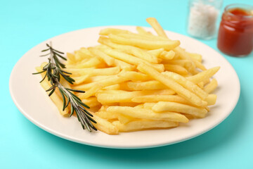 Plate with tasty french fries, ketchup and salt on light blue background