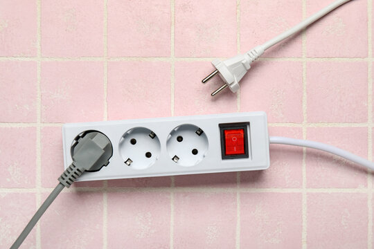 Electric extension cord with plugs on pink tile background