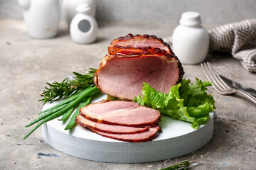 Board with tasty smoked ham and greens on grey grunge background