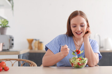 Young woman eating vegetable salad at table in kitchen