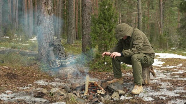 A man traveler sits by a campfire in a forest camp. The concept of tourism and living in the wild.