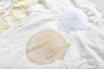 Laundry detergent with stained clothes on light background, closeup
