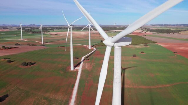 Close-up from above of wind turbines spinning in a row with bright sun and clear sky producing electricity natural energy. Numerous windmills turning in the background, Wind Power, Spain
