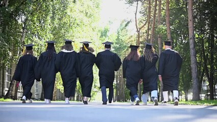 Rear view of a group of happy students in robes throwing academic caps into the air. Slow motion. 