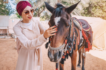 A young girl stands confidently beside her majestic Arabian horse, both of them bathed in the warm glow of the setting sun.