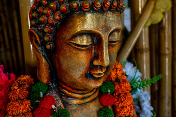 Close up of bronze buddha statue sitting in meditation with flower decorations for festival...