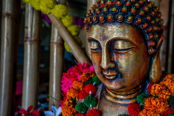 Close up of bronze buddha statue sitting in meditation with flower decorations for festival...
