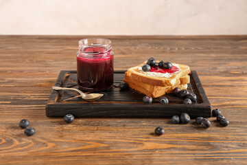 Wooden board of tasty toasts with blueberry jam on table