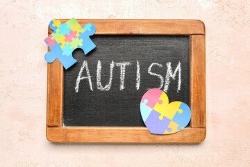 Chalkboard with word AUTISM, paper puzzle piece and heart on beige background
