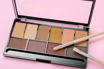 Palette of eyeshadows with brushes on pink background, closeup