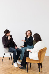 Concept of marital therapy. A female psychologist sits with her back to the camera and listens to the family couple during therapy session
