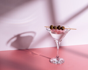 a martini glass with olives on a pink background and the shadows.