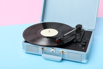 Record player with vinyl disk on table near pink wall