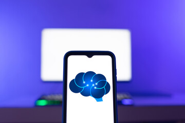 Smartphone displaying an illustration of a brain representing artificial intelligence, with a computer screen in the background. Artificial intelligence generating texts and images.