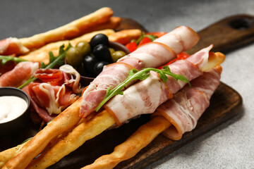 Wooden board of tasty Italian Grissini with bacon on grunge background, closeup