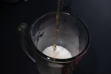 A stream of beer pours into a glass. Dark background.