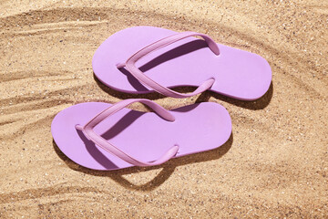 Fototapeta na wymiar Lilac flip-flops on sand, top view