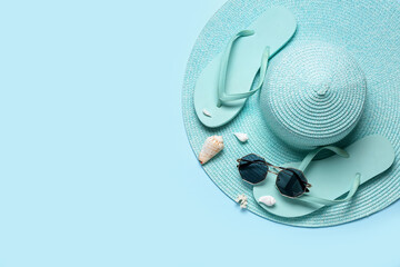Flip-flops with sunglasses, seashells and hat on blue background