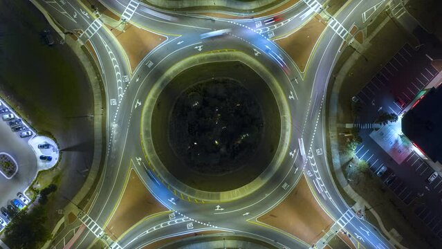 Top view of city street traffic on roundabout intersection at night with fast moving cars. Timelapse of illuminated urban circular transportation crossroads
