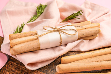 Wooden board with bunch of tasty Italian Grissini on pink background