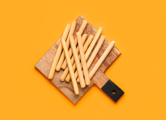 Wooden board with tasty Italian Grissini on orange background
