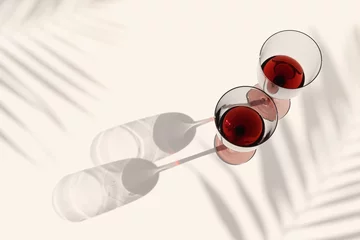 Deurstickers Minimal summer flat lay with glasses of red wine, sunlight shadow, palm leaf shade on beige background, Two wine glasses, alcohol drinks photo Holidays, parties, events, relaxation concept © yrabota