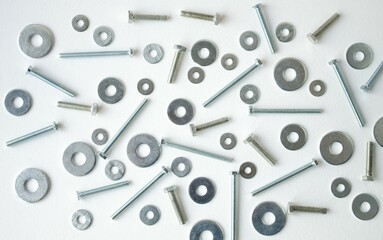 Close-up bolts, nuts and washers are scattered in a chaotic manner on a white background.  Flat lay top view, close-up.  Background with metallic elements.