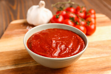Bowl with tasty tomato paste on wooden background, closeup