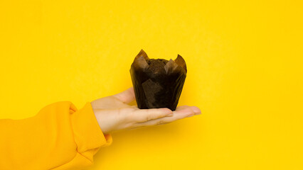 Female hand with a chocolate muffin on a yellow background with a place for a text