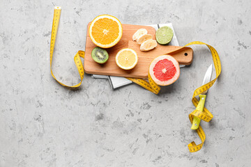 Wooden board with fruits and yellow measuring tape on grunge background. Diet concept