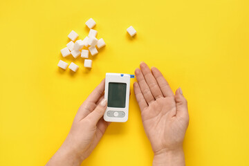 Diabetic woman with glucometer and sugar on yellow background
