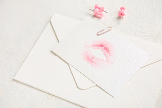 Envelope with lipstick kiss mark and paper clips on white background, closeup