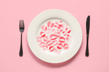 Plate with lipstick kiss marks and cutlery on pink background