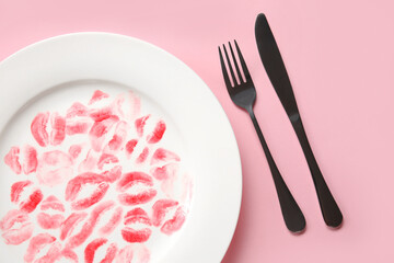 Plate with lipstick kiss marks and cutlery on pink background