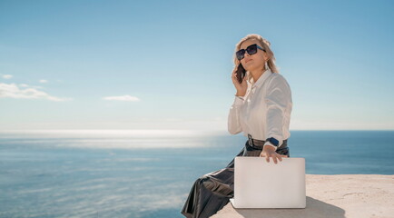 Freelance women sea working on a computer. Pretty middle aged woman with computer and phone outdoors with beautiful sea view. The concept of remote work.