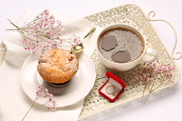 Tray with muffin, engagement ring, cup of coffee and flowers on white background, closeup