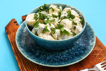Bowl of tasty Potato Salad with greens on blue background